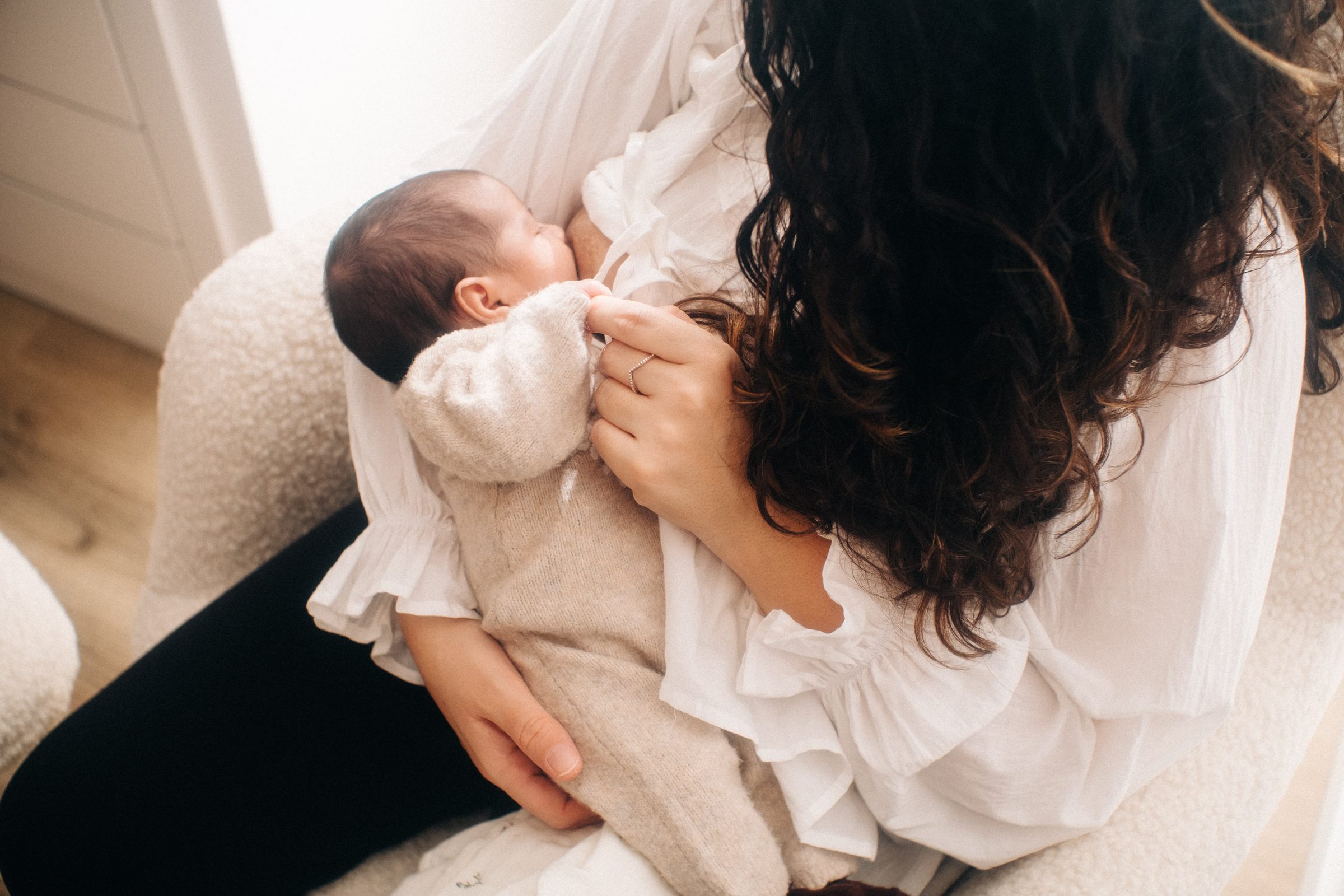 Mãe a alimentar o seu bebé numa poltrona creme, vista de cima