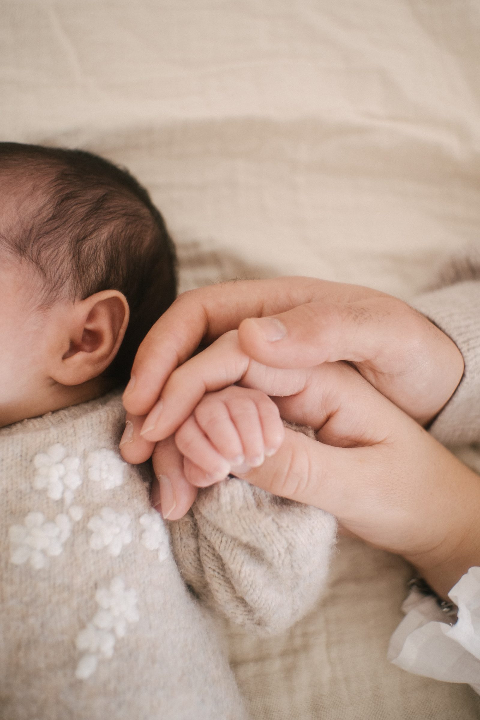 A mão pequena de um recém-nascido encaixada de manso nas mãos de um adulto